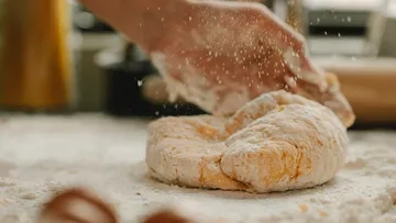 Hand knetet Teig in einer bemehlten Küchenszene.
