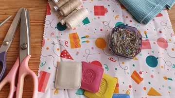 Tailor's tools lie on a colorful fabric table.