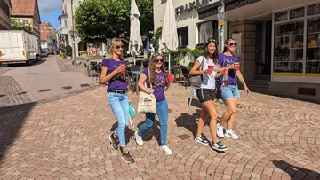 Vier Frauen gehen lächelnd auf einem gepflasterten Platz.
