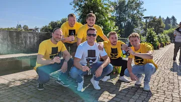 Sechs Männer in gelben Shirts sitzen im Freien zusammen.
