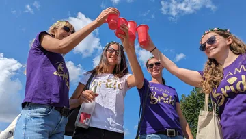 Four women raise red cups and celebrate outside.