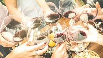 Glasses of red wine are raised together, festive atmosphere.