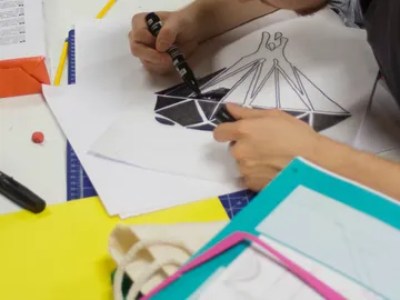 Ein Mensch zeichnet mit Stift auf Papier am Tisch.