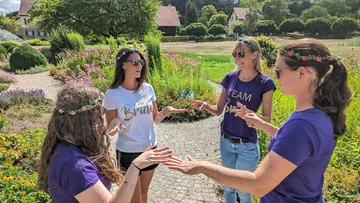 Vier Frauen spielen miteinander in einem Garten mit Blumen.