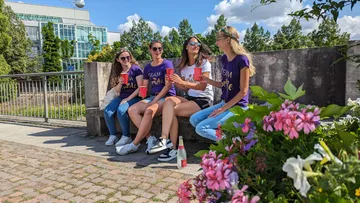 Vier Frauen sitzen lachend auf einer Steinbank im Freien.