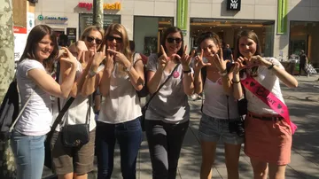 Sechs Frauen formen Herzen mit ihren Händen, lächeln fröhlich.