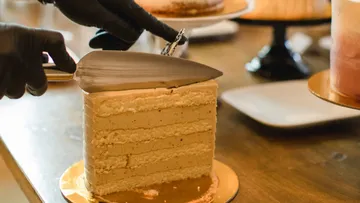 A hand cuts a piece of cake on a table.
