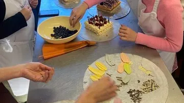 Chefs decorate cakes with berries and edible decorative leaves.