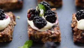 Kekse mit Sahne und Brombeeren auf dunklem Untergrund.