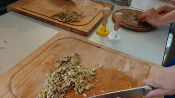 Schneidebrett, Gemüse wird klein geschnitten, Küche im Hintergrund.