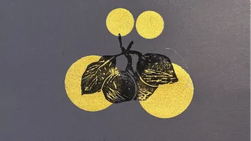 Eine schwarze Frucht mit Blättern vor einem goldenen Hintergrund.