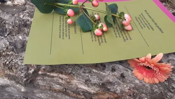 Blatt mit Gedicht und Blumen auf Holzuntergrund.