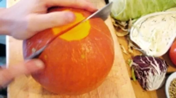 A hand cuts a pumpkin on a table.