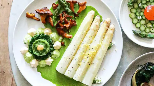 White asparagus with green sauce and mushrooms on a plate.