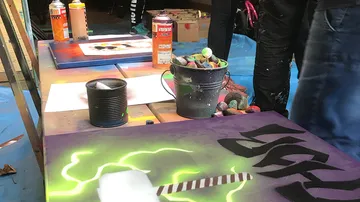 Paint cans stand on a table while people paint.