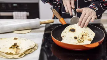 Eine Person brät Fladenbrot in einer Pfanne, Küche.