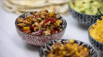 Eine Schüssel mit gewürztem Hähnchen und Gemüse auf Tisch.