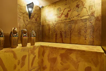 Egyptian figures stand in front of wall-filling hieroglyphs and paintings.