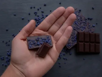 Dark chocolate lies on a table in one hand.