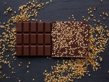 Dark chocolate lies on a dark background, surrounded by nuts.