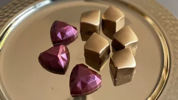 Square and heart-shaped chocolates lie on a golden plate.