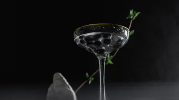 Ein Glas mit Flüssigkeit und Beeren steht vor dunklem Hintergrund.