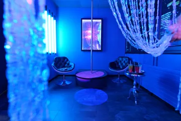 Blauer Raum mit Tisch, Stühlen und Tanzstange in der Mitte.