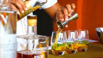 A bartender pours drinks into glasses on a counter.