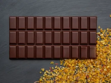 Chocolate bar is lying on a black background, surrounded by salt.
