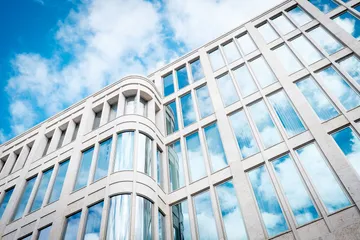 Modern façade reflects sky and cloud structures.