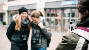 Two women pose laughing while another takes pictures.