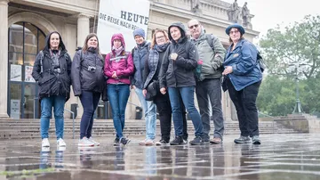 Group of people stand in front of a building in the rain.