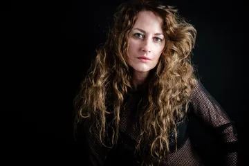 Woman with curly hair posing against black background.