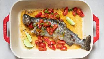 Ein Fisch liegt auf Tomaten in einer Auflaufform.