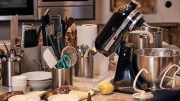 Food processor stirs dough in a messy cooking environment.