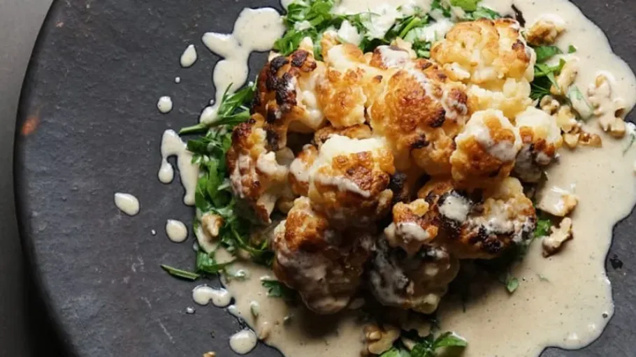 Roasted cauliflower sits on fresh green vegetables surrounded by sauce.