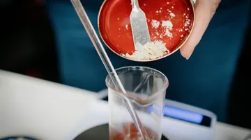 Ein Löffel Pulver wird in ein Glas gegossen.