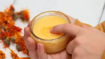 Hand hält Glas mit gelber Creme, Finger taucht ein.