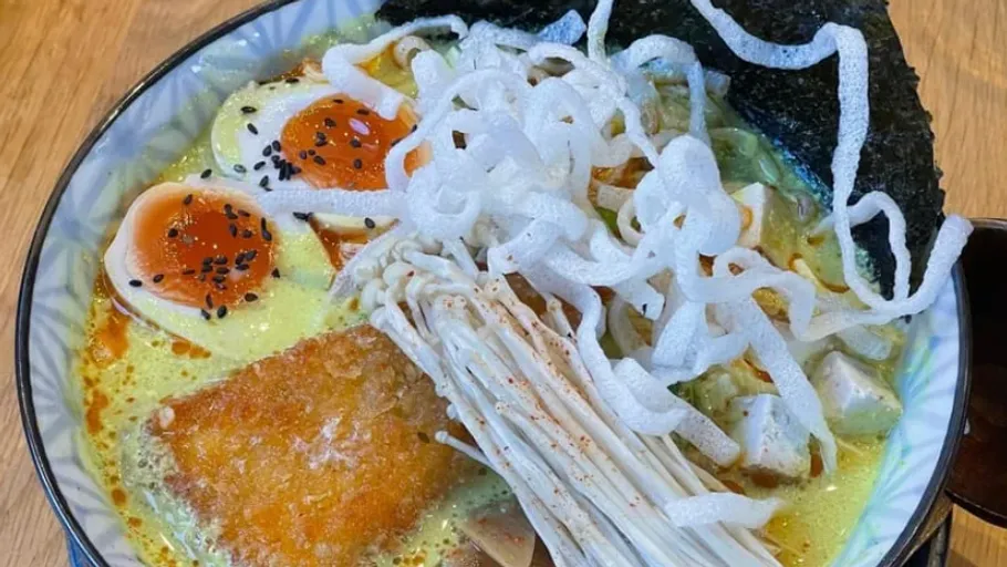 Bowl of ramen topped with egg, fish and vegetables.