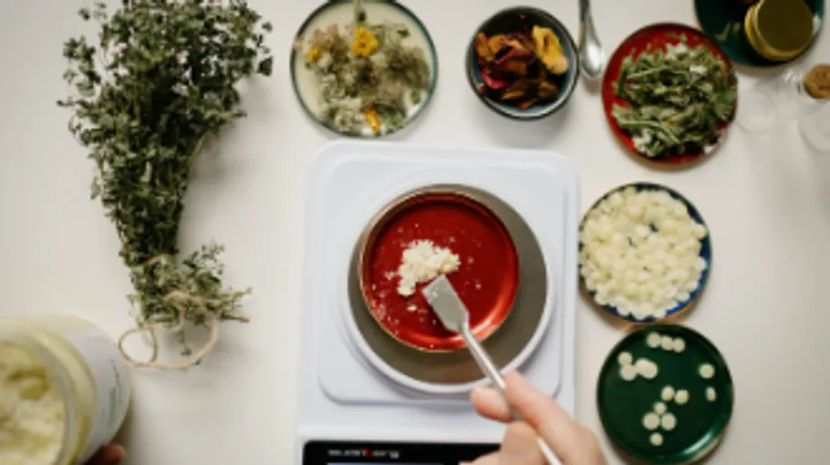 Herbs are weighed and mixed in a red bowl.