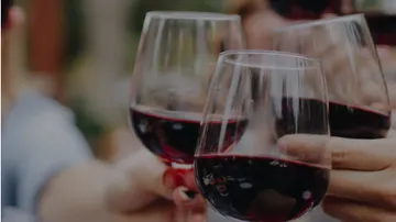 Glasses of red wine are raised to toast.