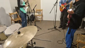 Musiker spielen Instrumente in einem Proberaum mit Stühlen.