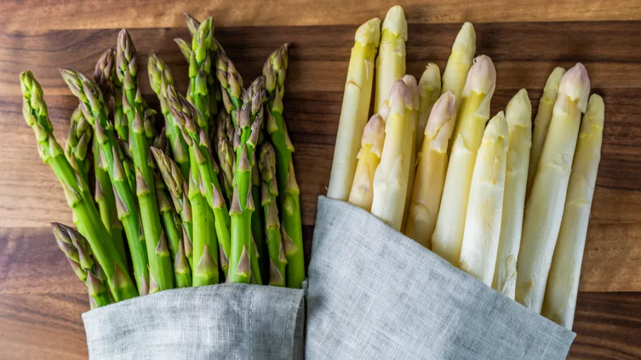 Green and white asparagus lie on a wooden board.