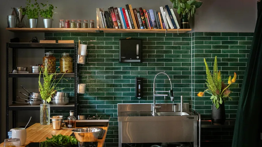 Kitchen decorated with green tiles, sink and plants.