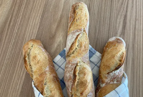 Three baguettes lie on a checkered tea towel.