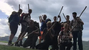 Group of people posing with sticks under cloudy sky.