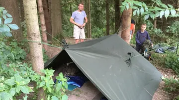 The tent is set up in the forest by two people.