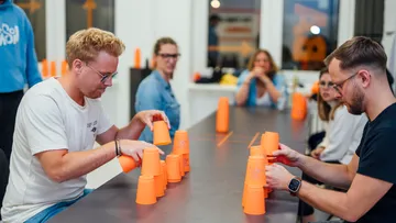 Two men are stacking orange cups at a table.