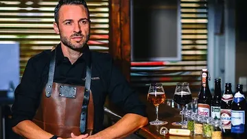 Bartender sits at the counter with drinks in the background.