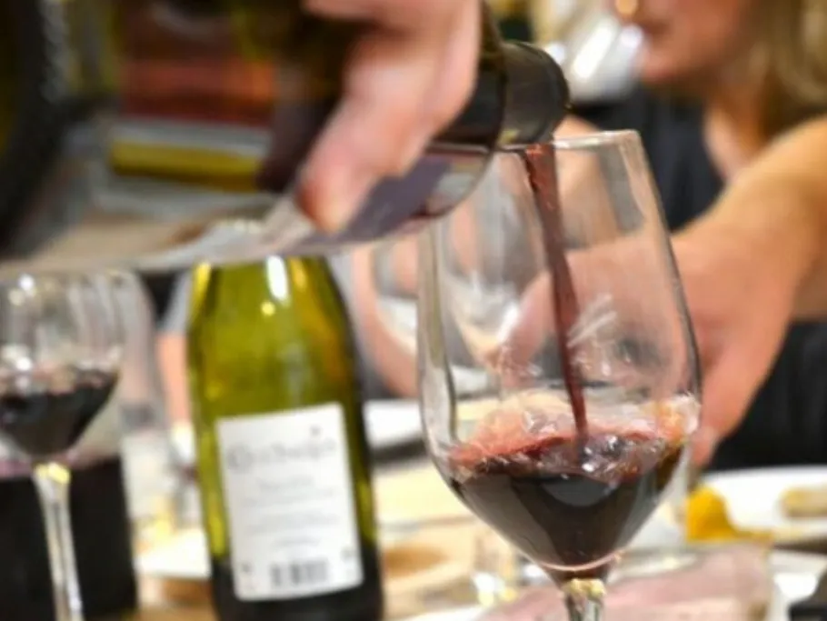 Red wine is poured into a glass surrounded by guests.
